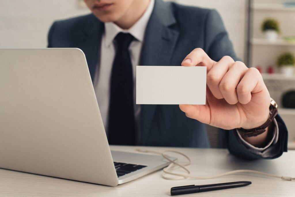 partial view of businessman holding white business card while using laptop